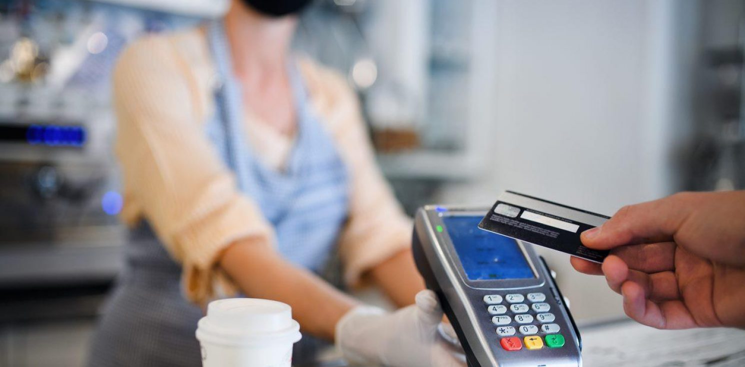 A contactless payment being made over a counter for a drink with the seller wearing PPE mask and gloves