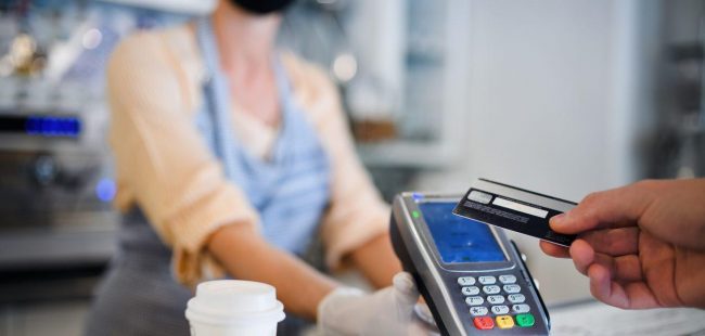 A contactless payment being made over a counter for a drink with the seller wearing PPE mask and gloves