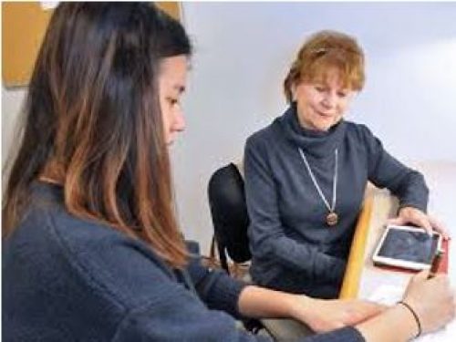two people sitting at a table using digital devices conversing with each other on their use